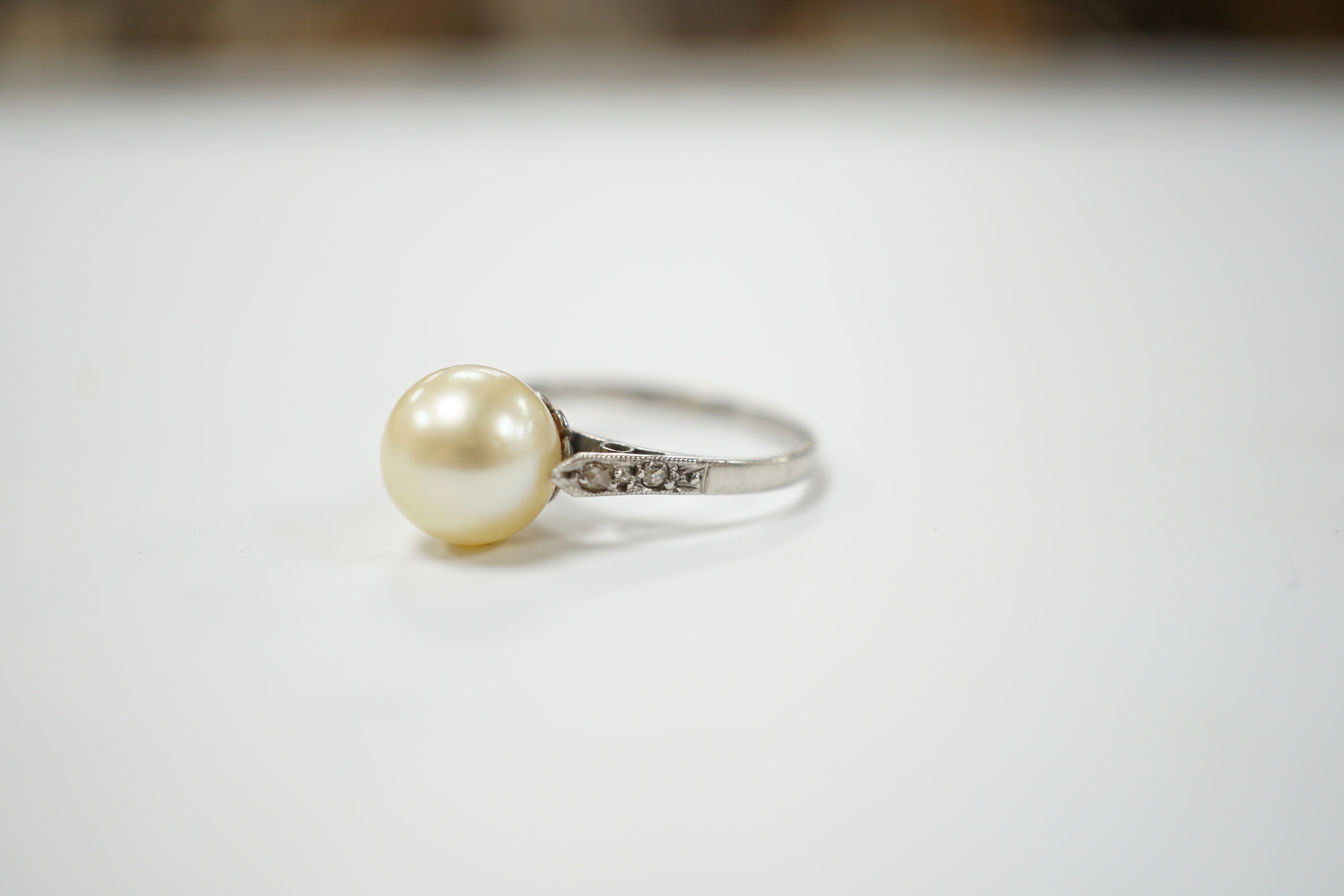 A white metal solitaire cultured pearl ring with diamond set shoulders, size J